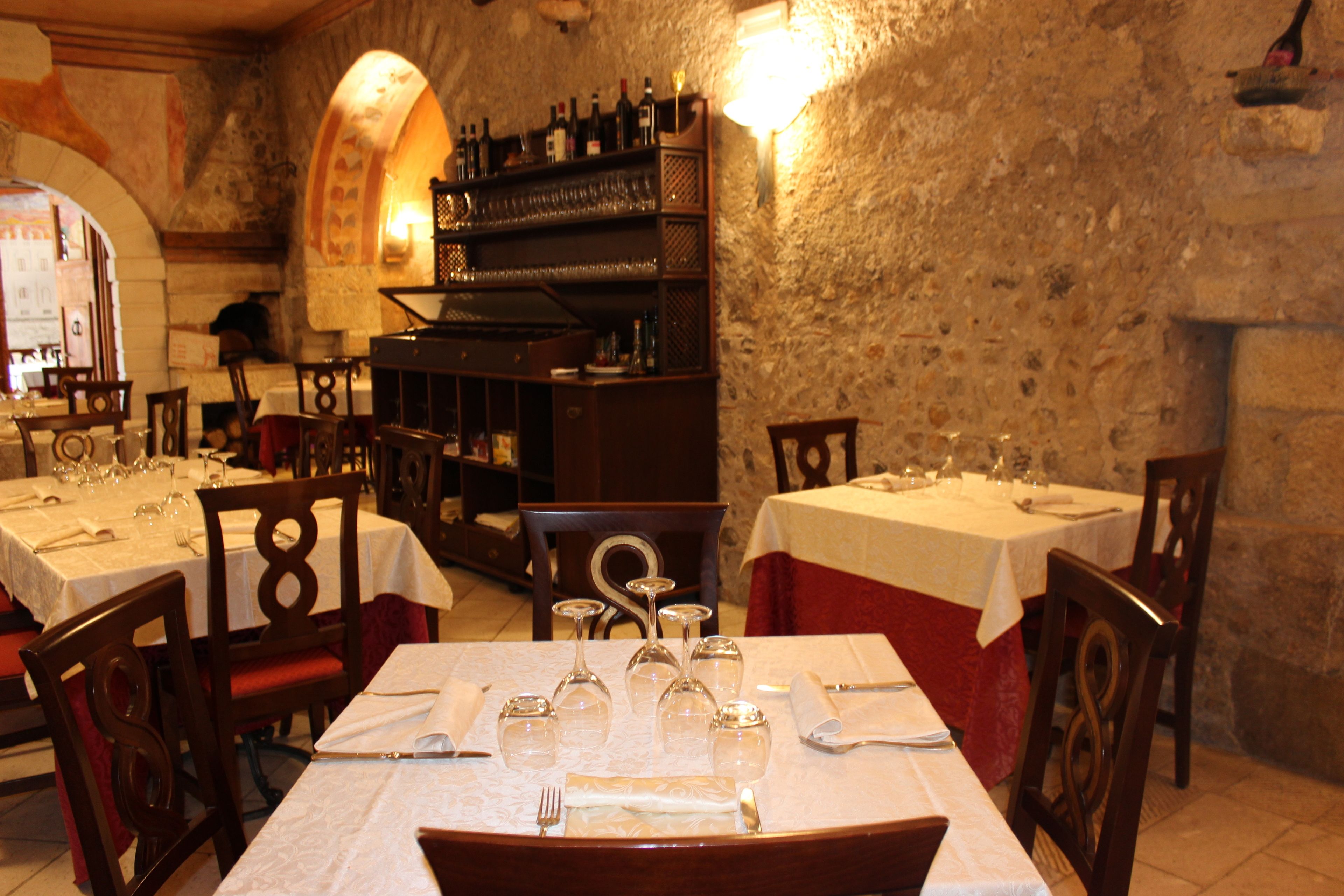 A restaurant with tables set for dining, wine glasses, and a bar area with bottles.