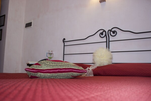 A bed with a metal headboard, a red bedspread, and decorative pillows.