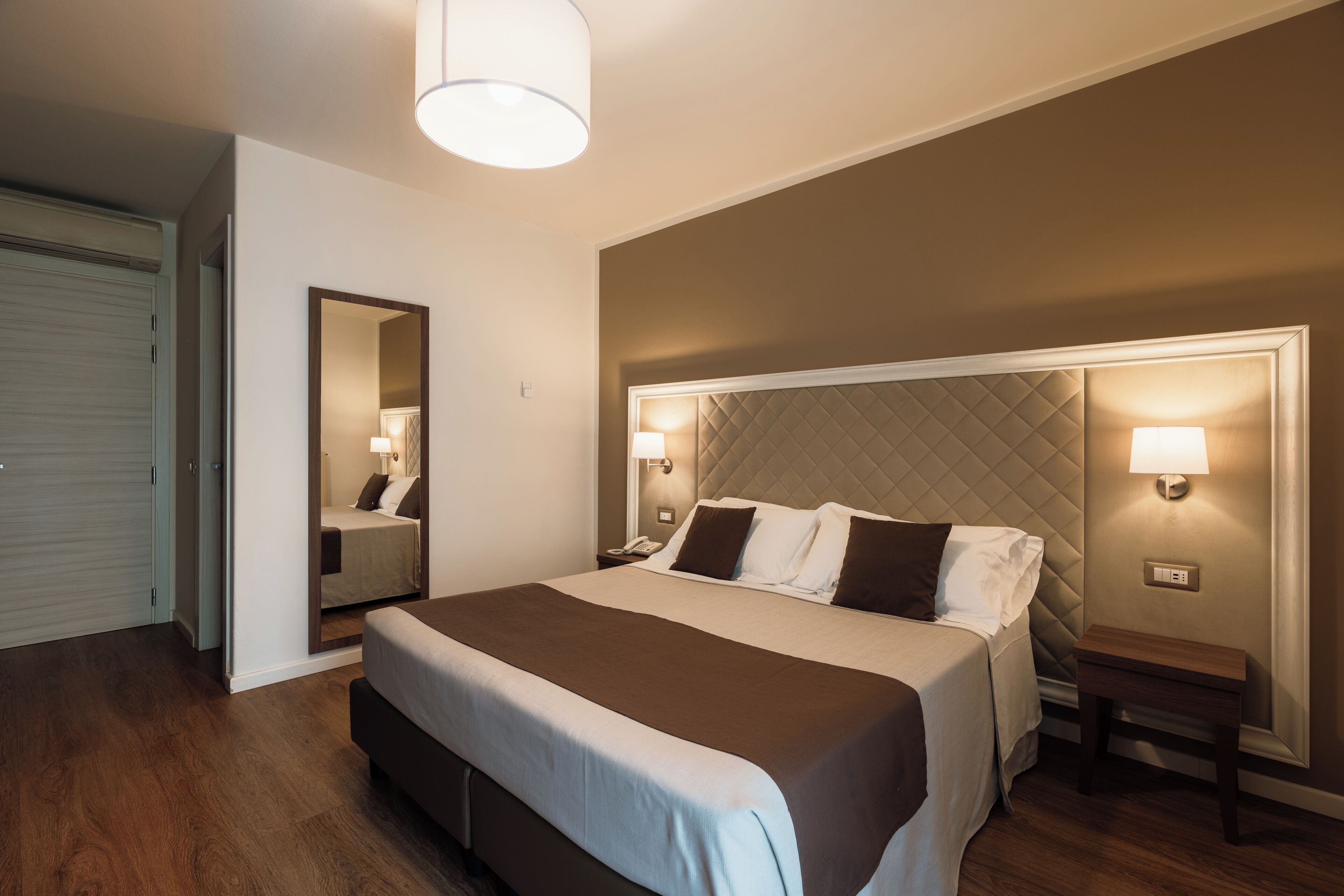 A hotel room with a large bed, bedside lamps, a nightstand, and a mirror.