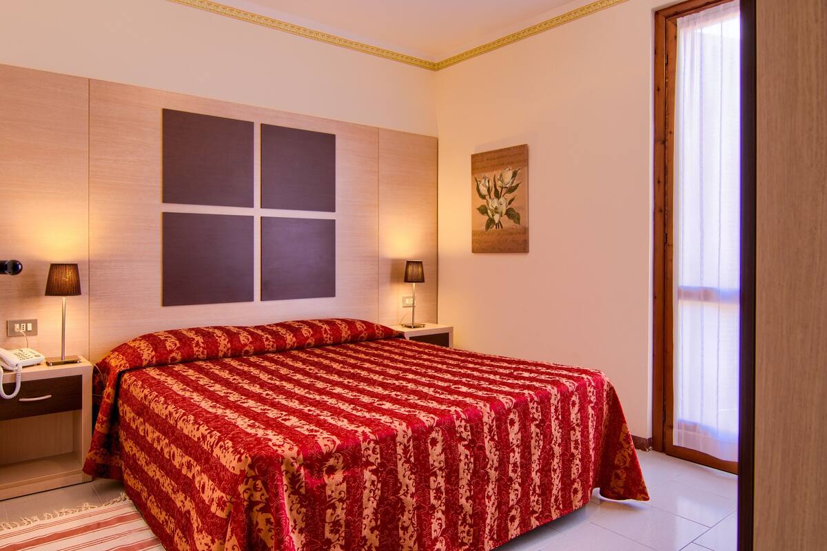 Habitación de hotel con una cama grande, dos mesitas de noche, un teléfono y una ventana con cortinas.