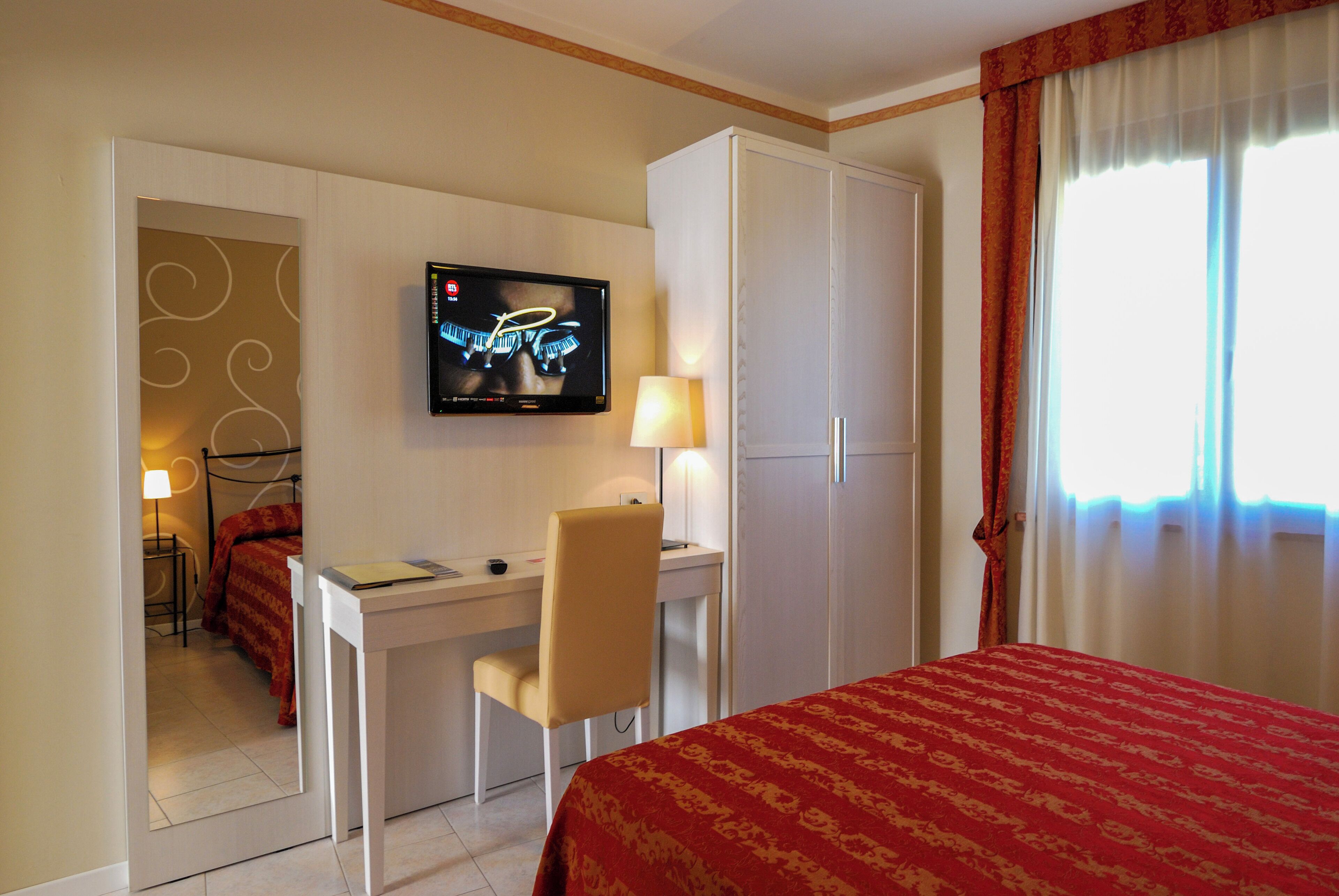 A hotel room with a bed, a desk with a chair, a television, and a wardrobe.