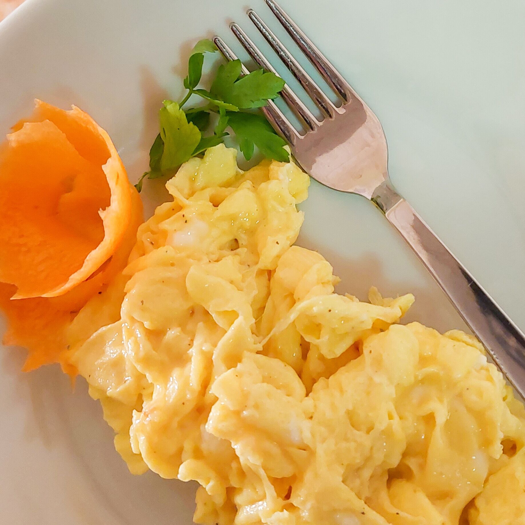 Scrambled eggs with a side of orange slices and parsley on a plate.