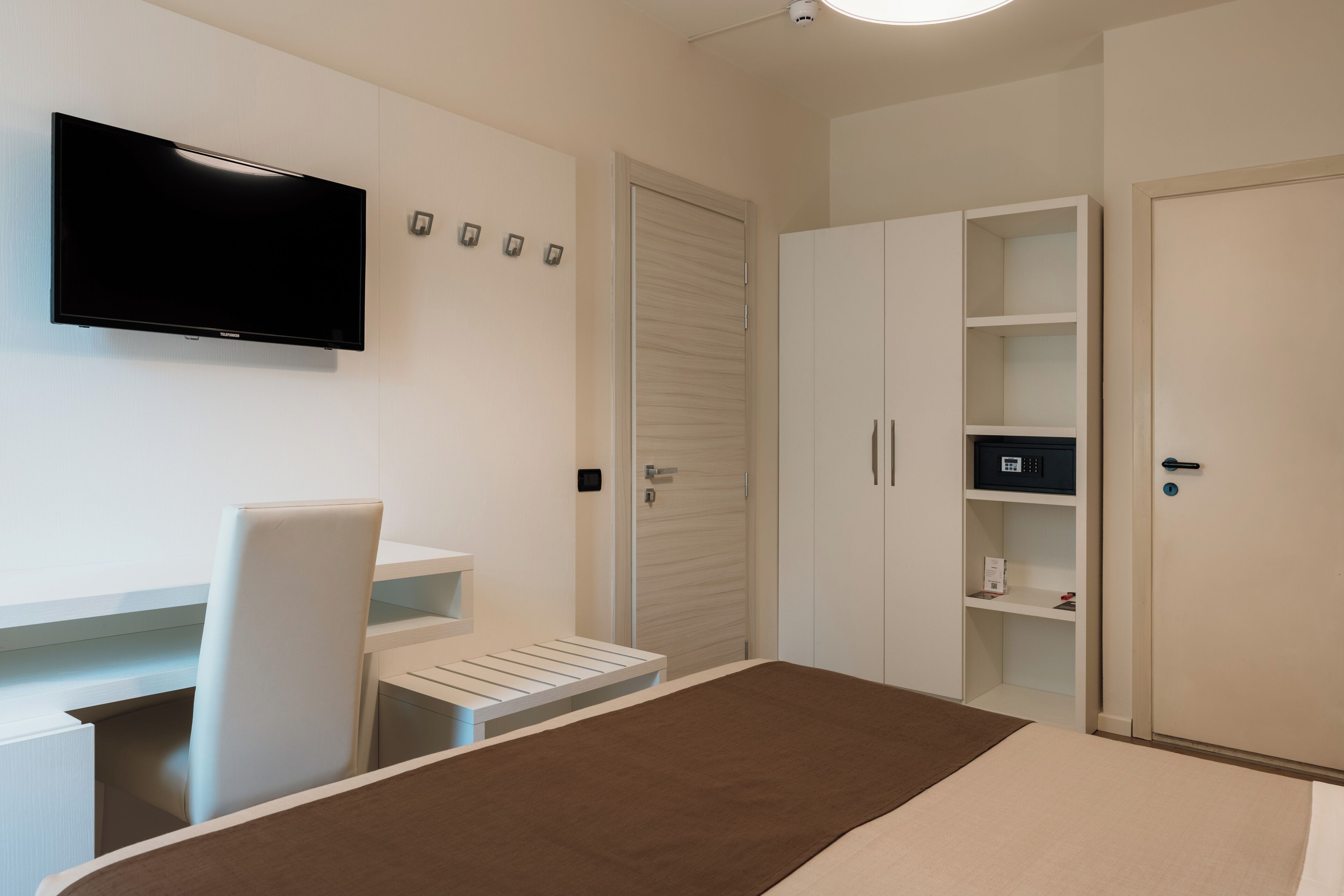 Habitación de hotel con cama, escritorio con silla, televisor en la pared y armarios empotrados.