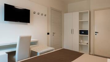 Habitación de hotel con cama, escritorio con silla, televisor en la pared y armarios empotrados.