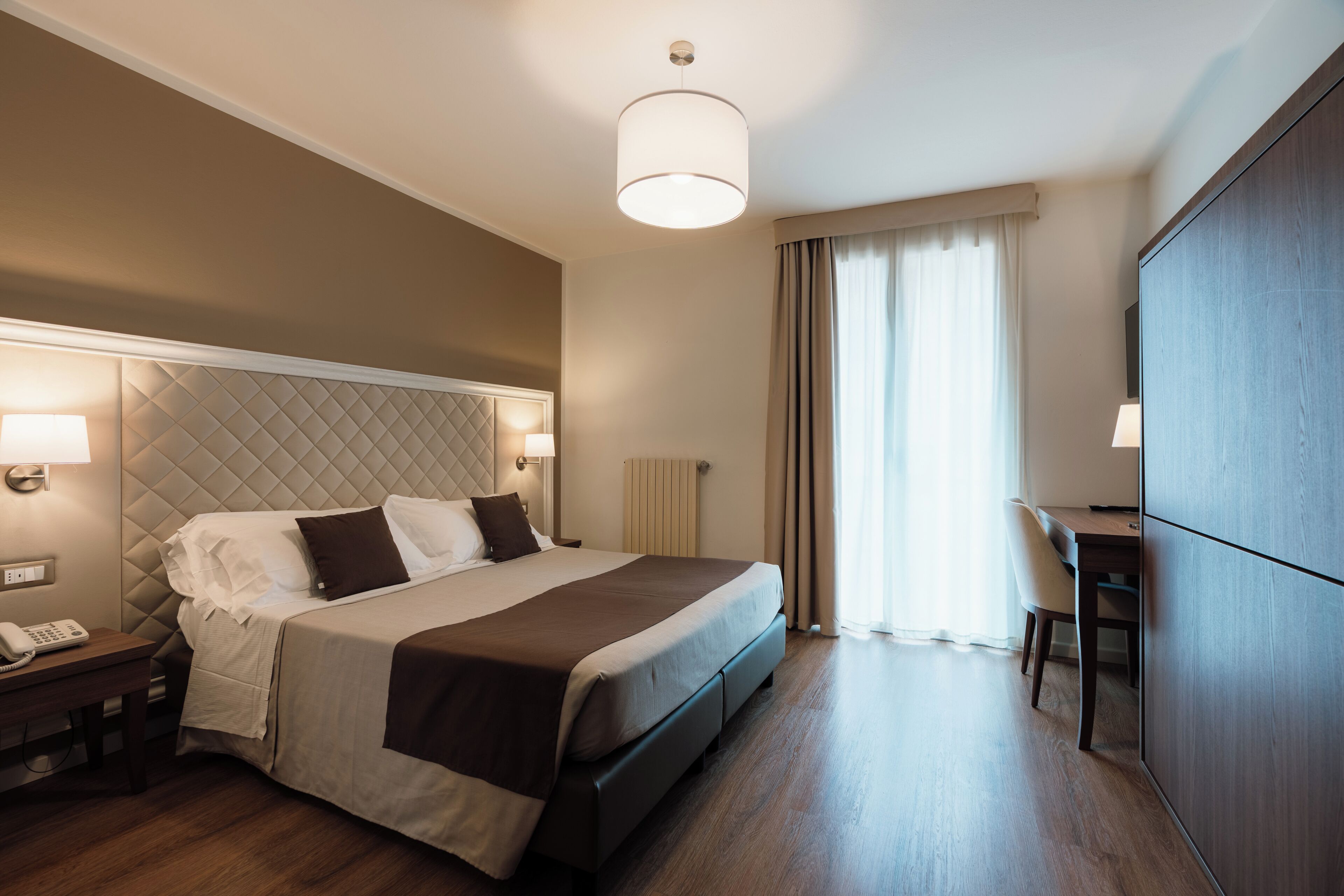 Ein Hotelzimmer mit einem Bett, Nachttischlampen, einem Schreibtisch und einem großen Kleiderschrank.