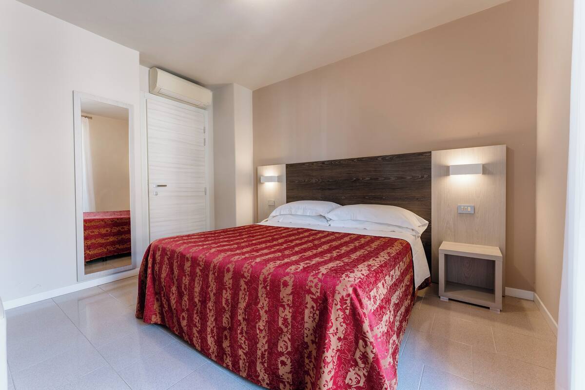 Un dormitorio con una cama grande, cabecera de madera, lámparas de noche y colcha estampada roja.