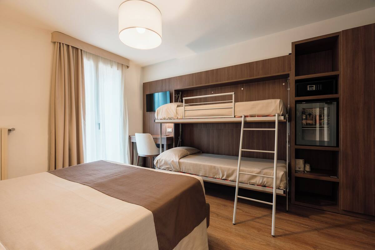 Una habitación de hotel con literas, un escritorio, una silla, un televisor y un armario.