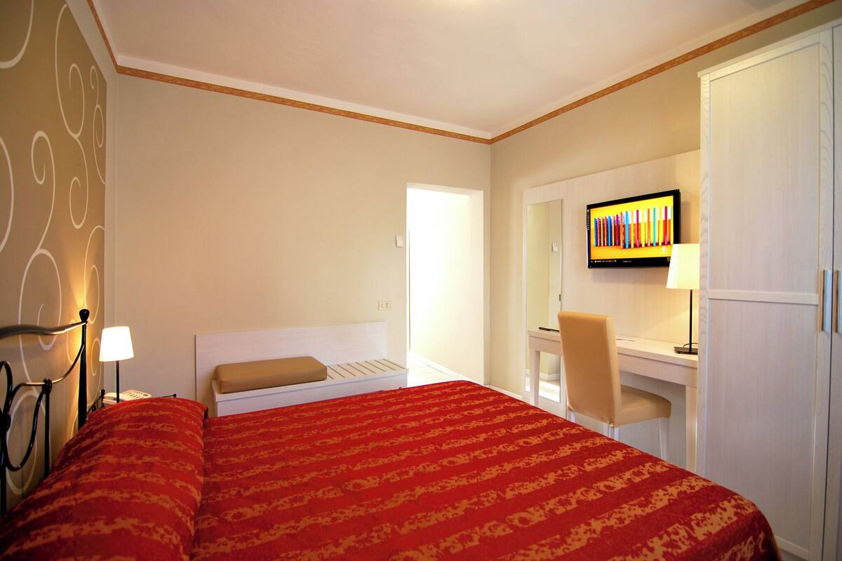 Una habitación de hotel con cama, escritorio, silla, televisor y armario.