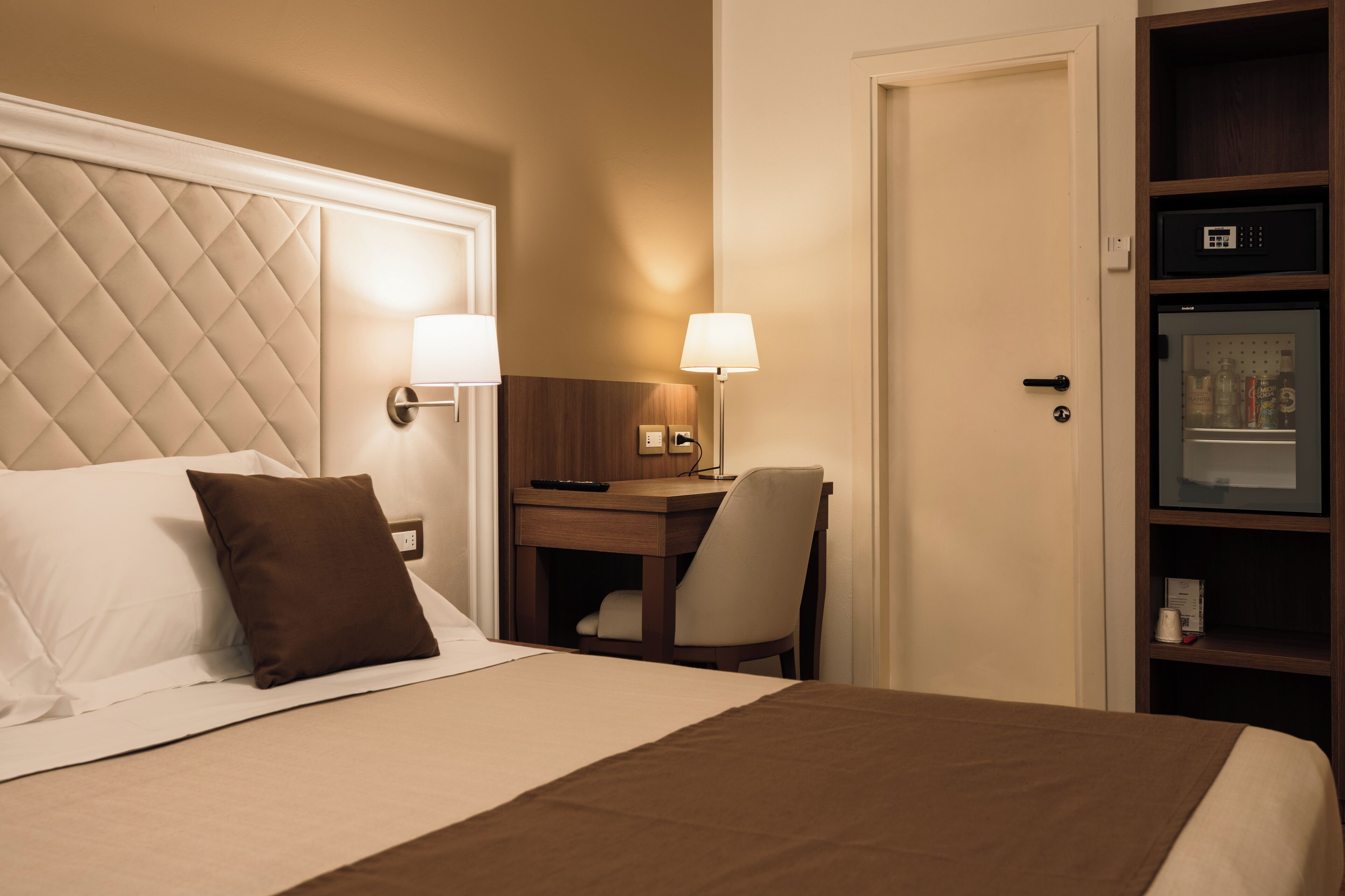 A hotel room with a bed, a desk, a chair, a nightstand, and a minibar.