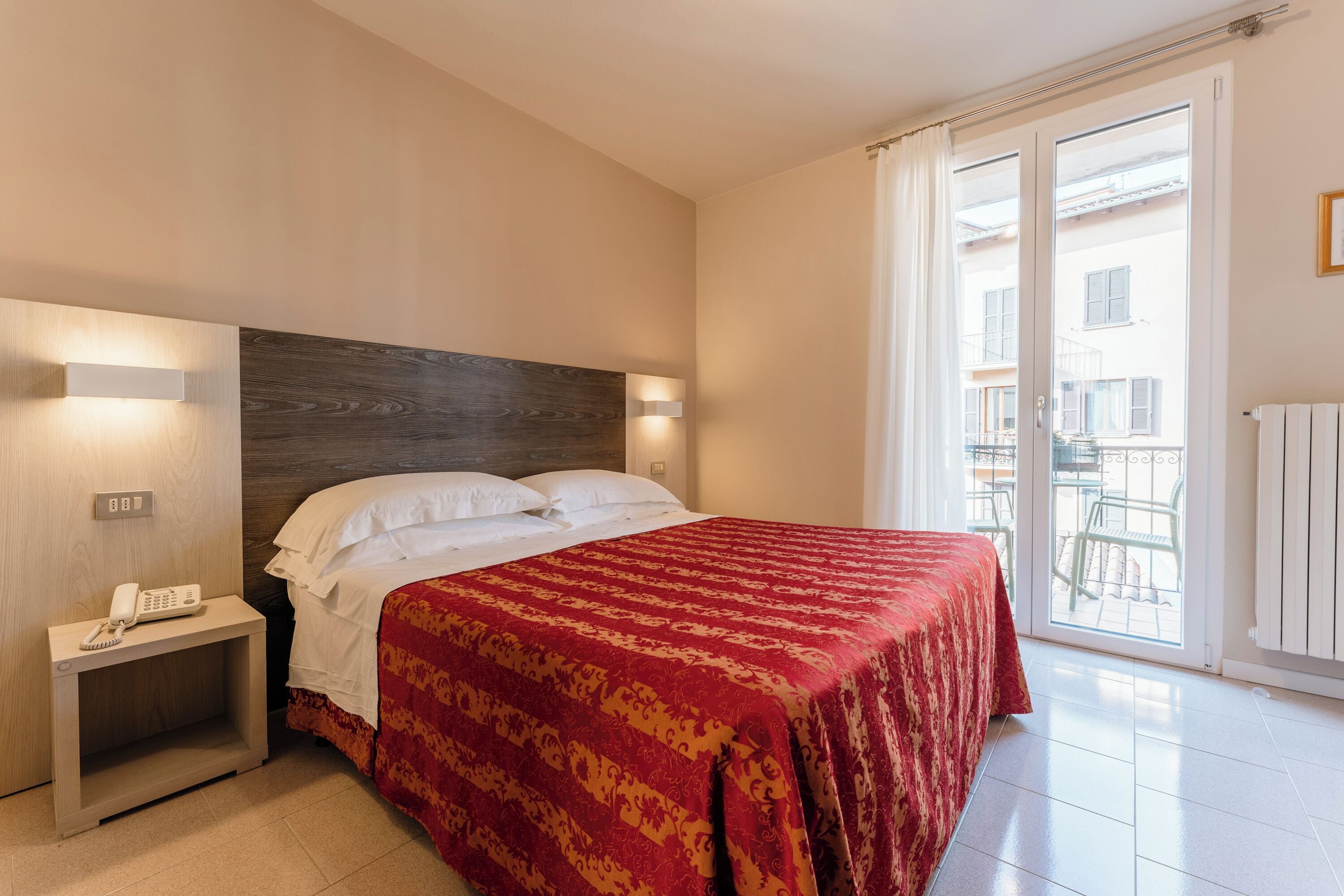 Una camera d'hotel con un letto, un comodino e vista sul balcone.