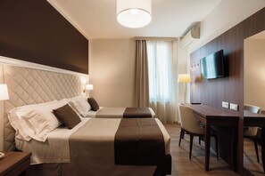 Een hotelkamer met twee bedden, een bureau, een televisie en een raam met gordijnen.