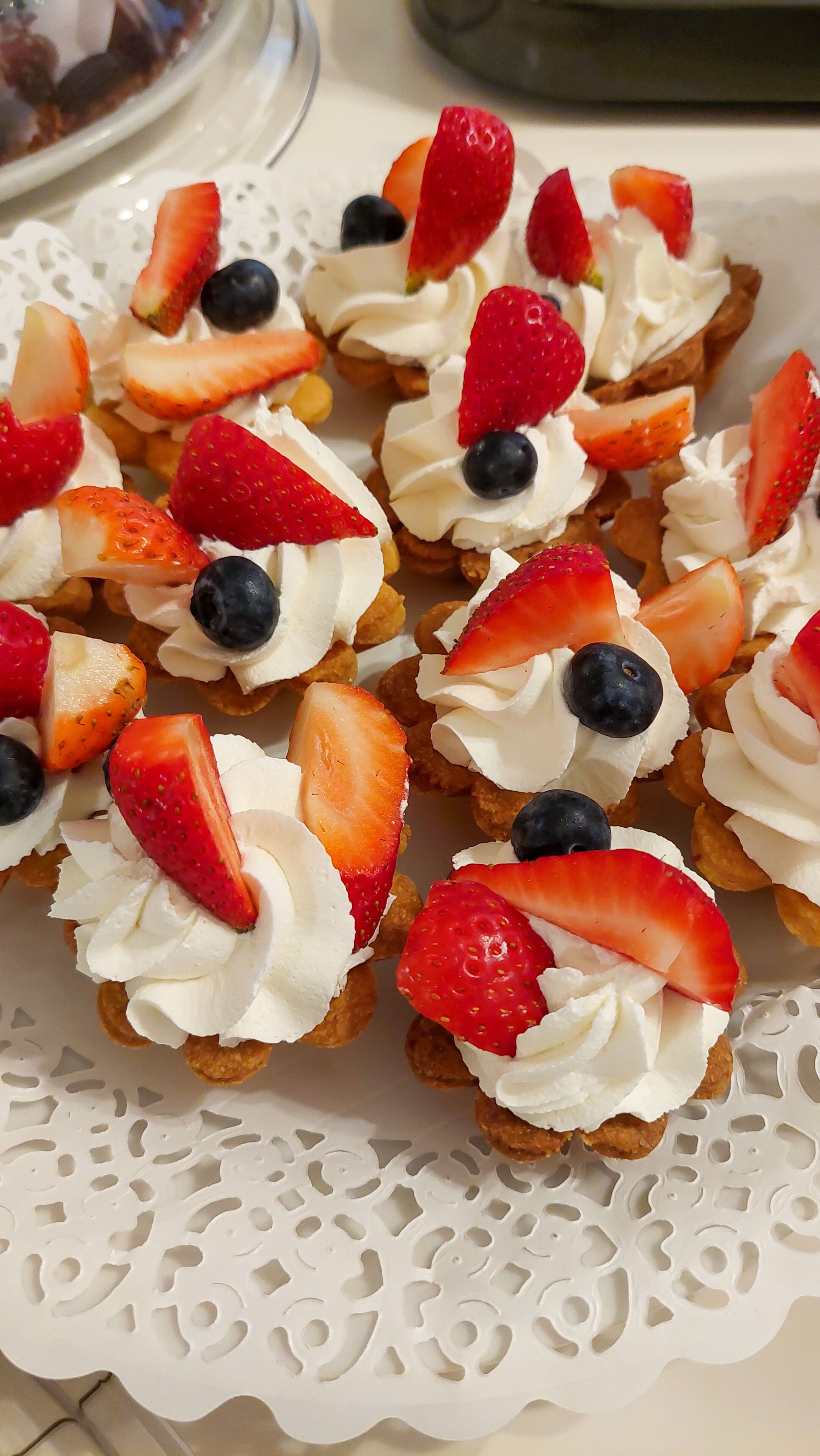 Une assiette de pâtisseries garnies de fruits, posée sur une nappe en dentelle blanche.