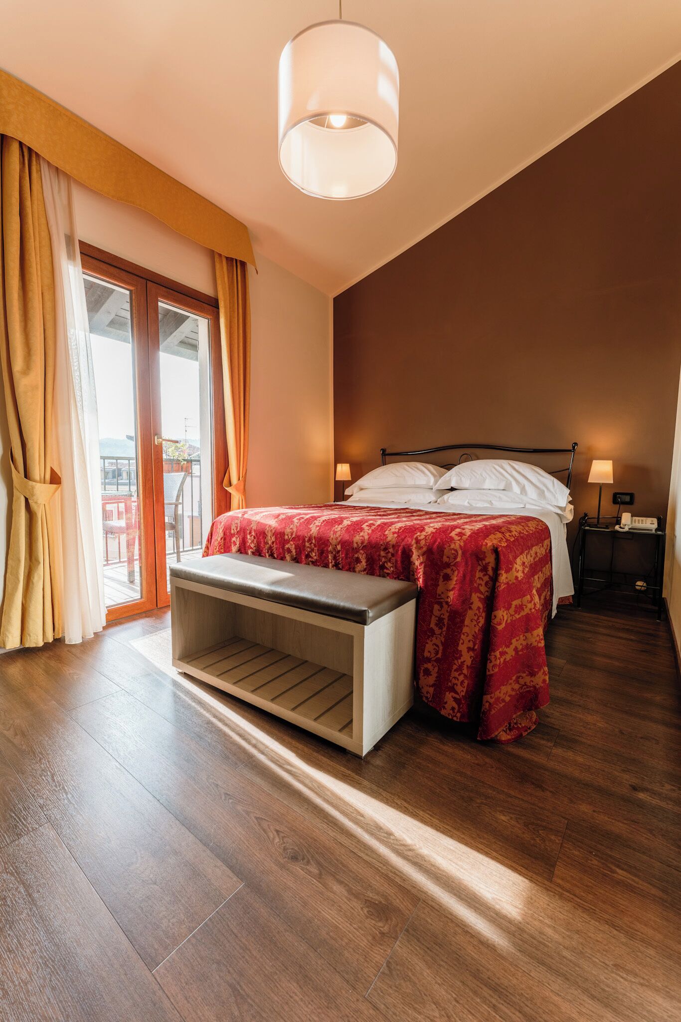 Un dormitorio con cama, lámparas de noche, un banco y vistas al exterior.