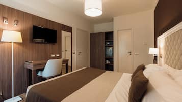A hotel room with a bed, desk, chair, TV, wardrobe, and a lamp.