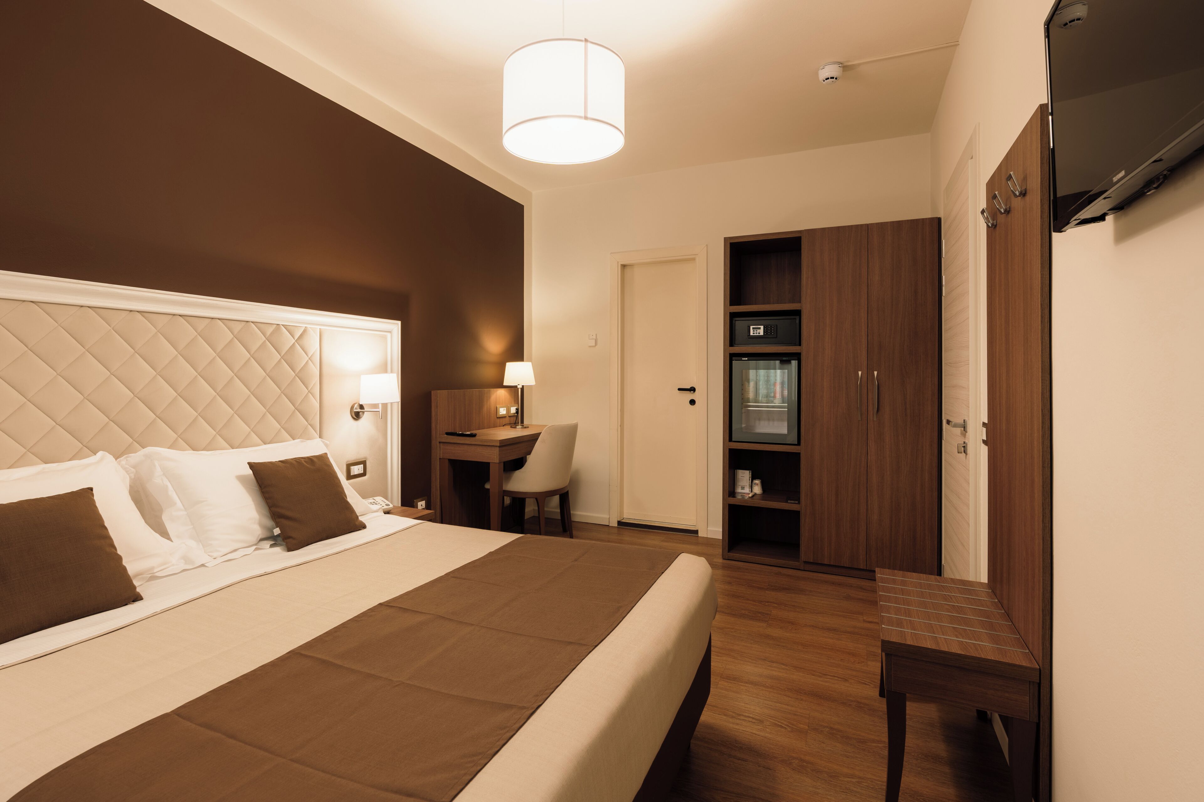 A hotel room with a bed, desk, chair, wardrobe, and a television.