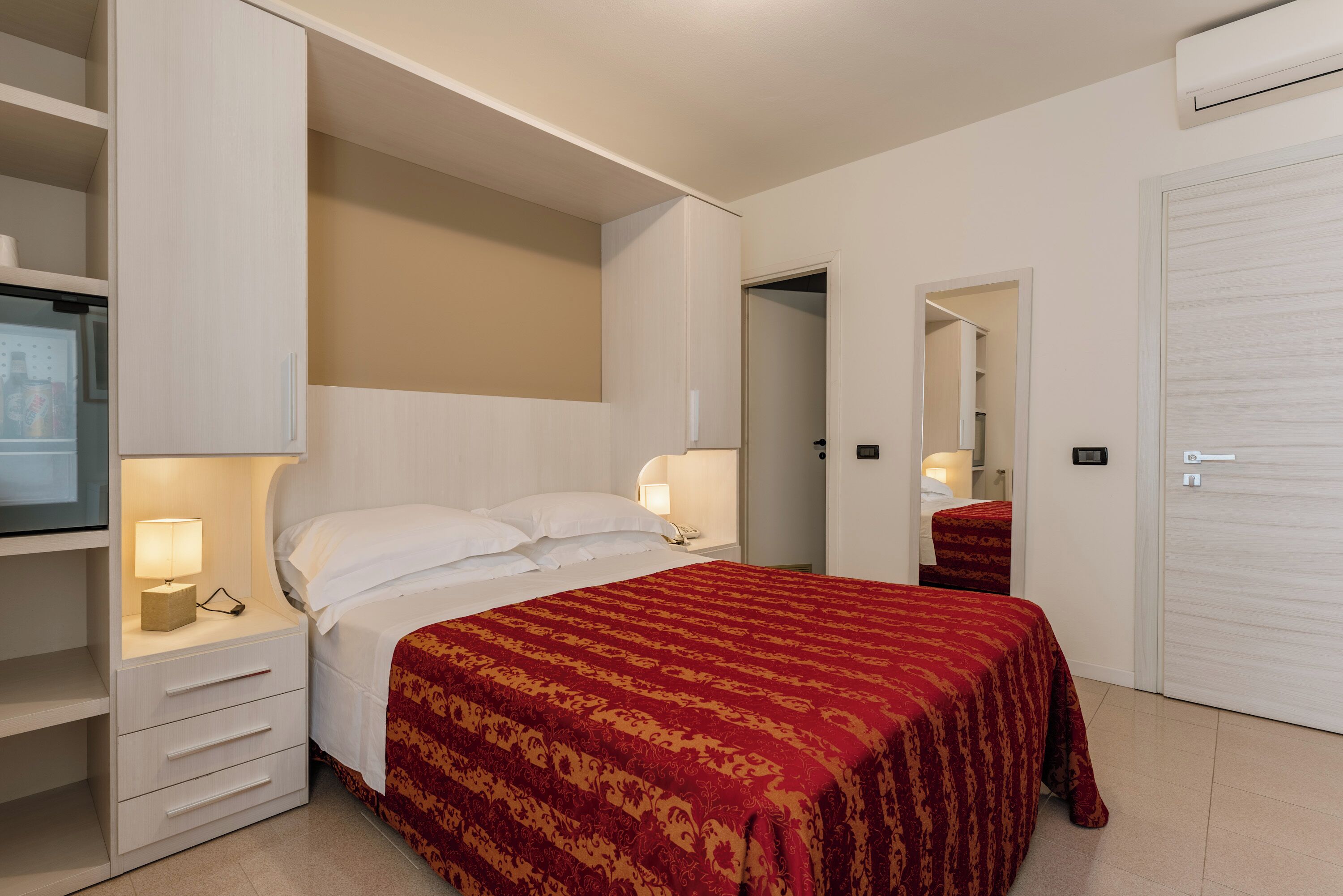 Una habitación de hotel con cama, mesita de noche, armario y espejo.