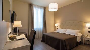 Een hotelkamer met een bed, nachtkastjes, een bureau met lamp, een stoel, een spiegel en een raam met gordijnen.