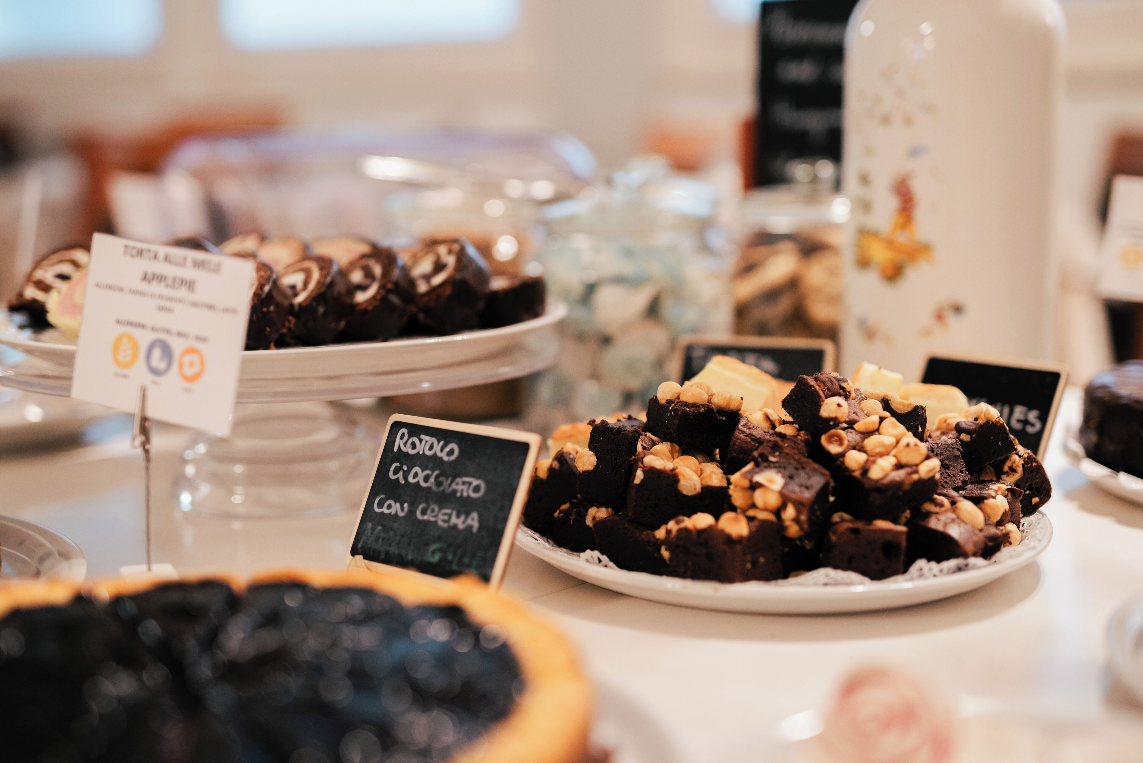 A dessert display with various types of cakes and pastries, including a sign indicating a chocolate cake with cream.