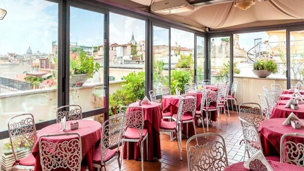 Un restaurante en la azotea con mesas y sillas, amplios ventanales con vistas a la ciudad.