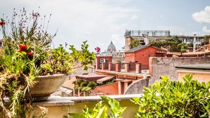 Un balcón con mesa lista para el desayuno, que incluye croissants, café y jugo, con vistas a un paisaje urbano con edificios y un templo.