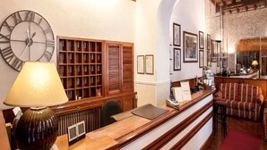 Un área de recepción con un escritorio de madera, un reloj, una lámpara, una estantería y cuadros en la pared.