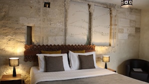 A bedroom with a stone wall, a wooden headboard, a bed with white and brown bedding, two bedside lamps, and a chair.