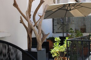 A wooden sculpture, a black chair, a potted plant, and a large umbrella. - La Banasterie (Avignon)