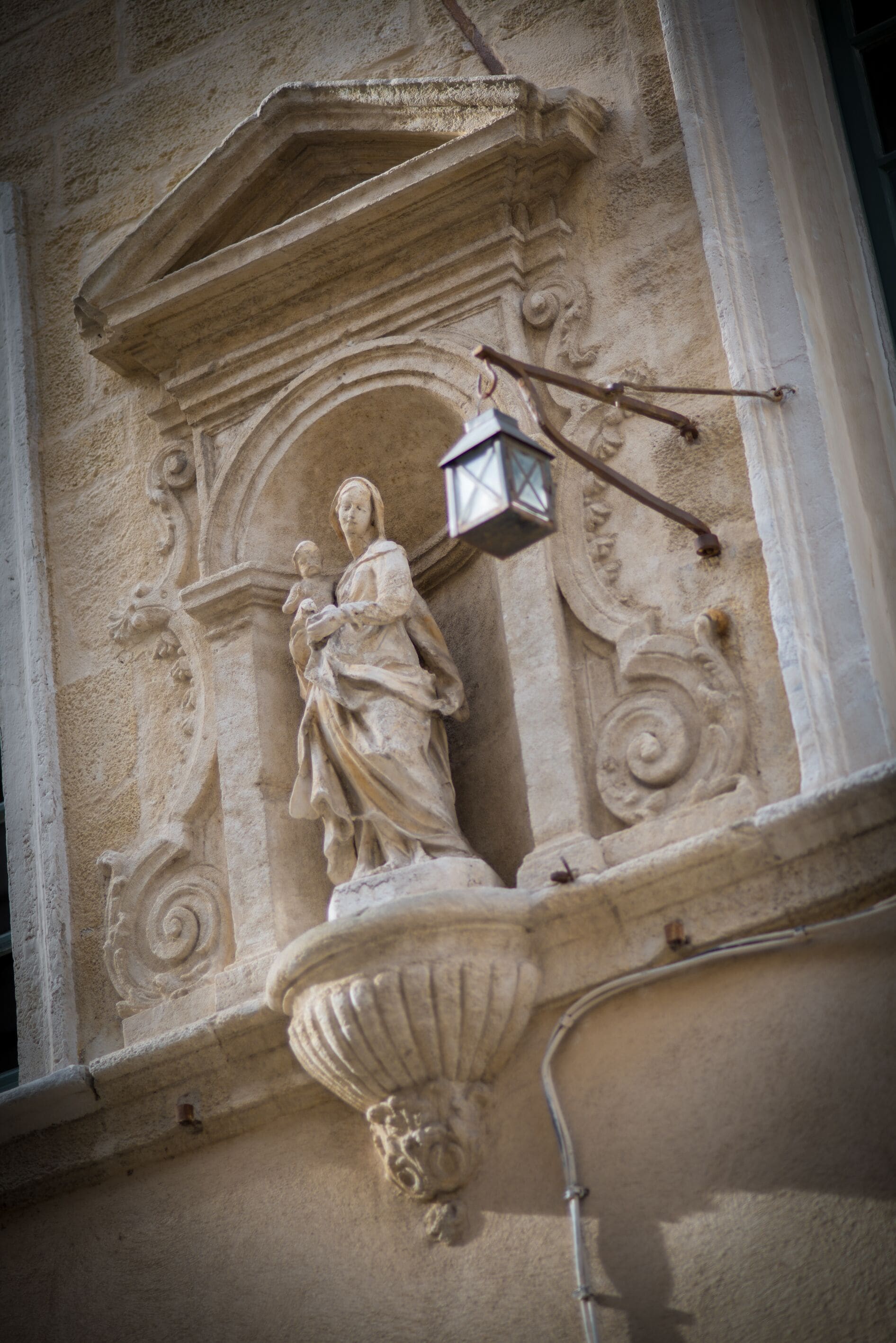 Fachada de piedra con un relieve que muestra a una mujer sosteniendo a un niño, un farol y detalles arquitectónicos ornamentales.