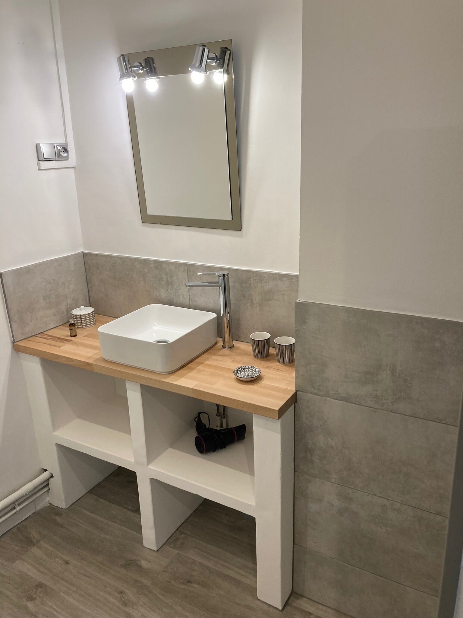 Une salle de bain moderne avec un lavabo blanc, un miroir avec éclairage intégré et un meuble-lavabo en bois.