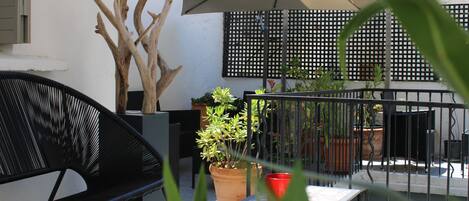An outdoor patio area with a black chair, a table, a potted plant, and an umbrella.