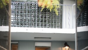 A two-story building with a balcony, a door leading to an interior room, and a small outdoor plant.