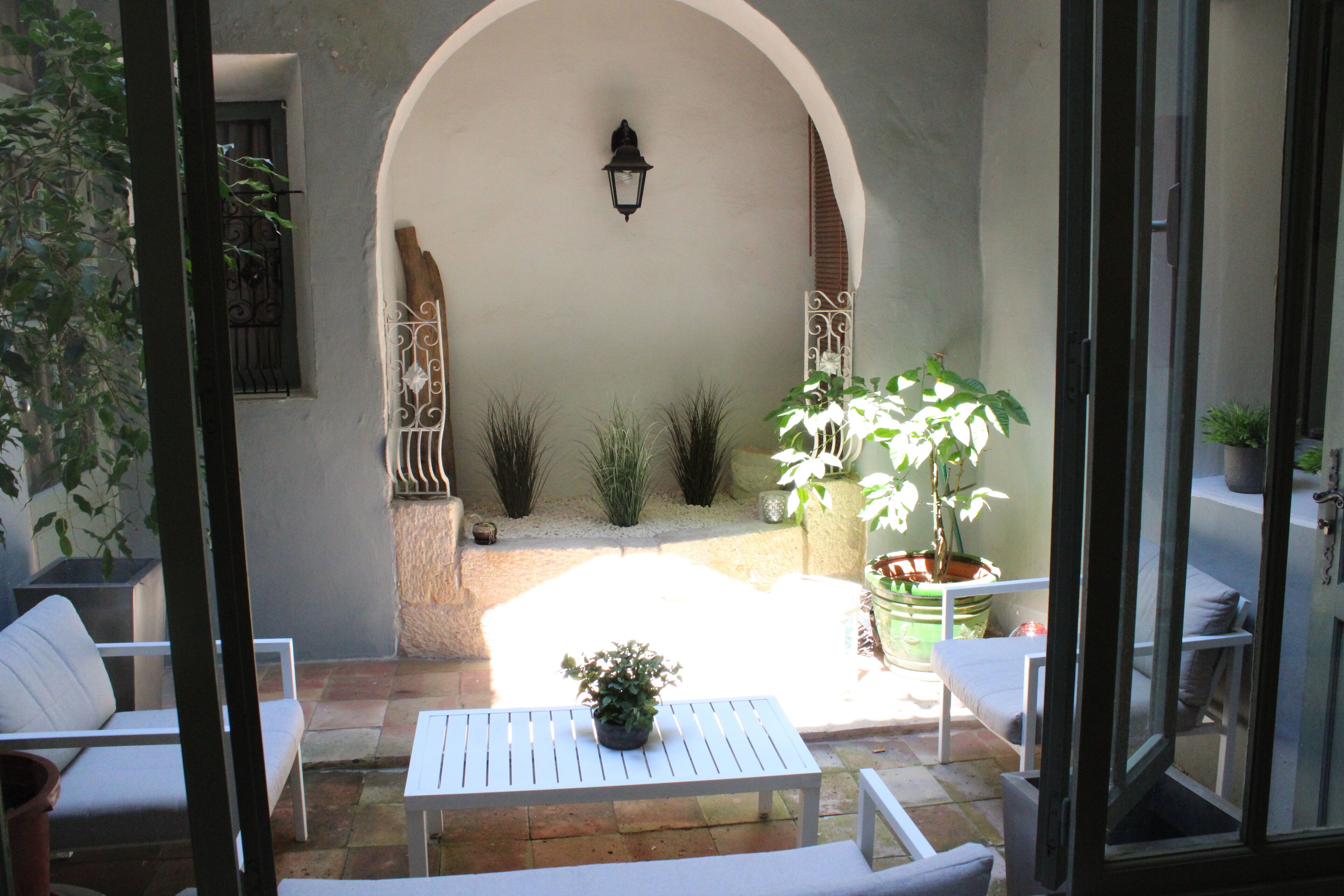 A patio with a white table and chairs, surrounded by potted plants and a decorative archway.