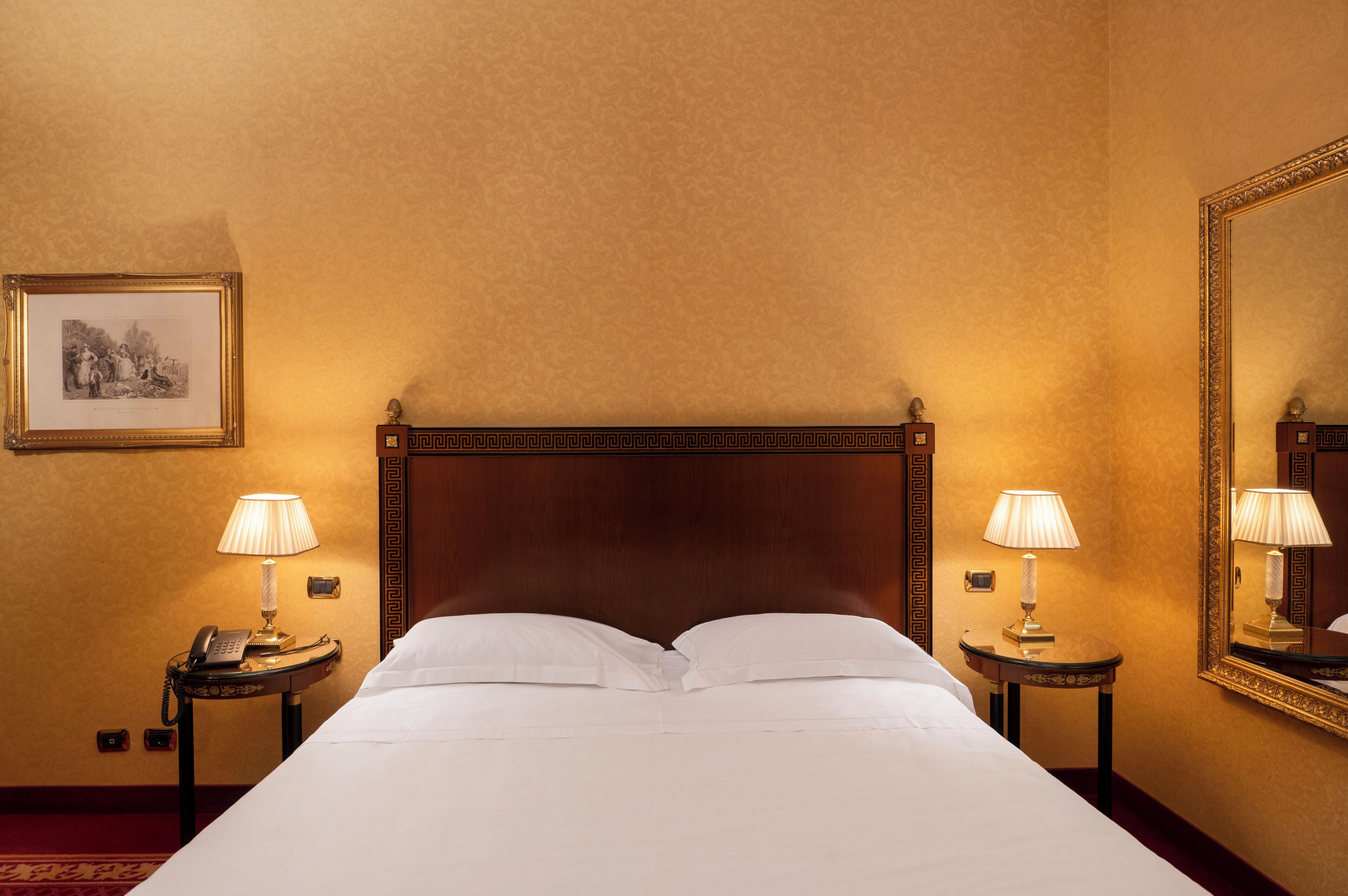 A hotel room with a large bed, two bedside tables with lamps, a framed picture on the wall, and a mirror on the right.