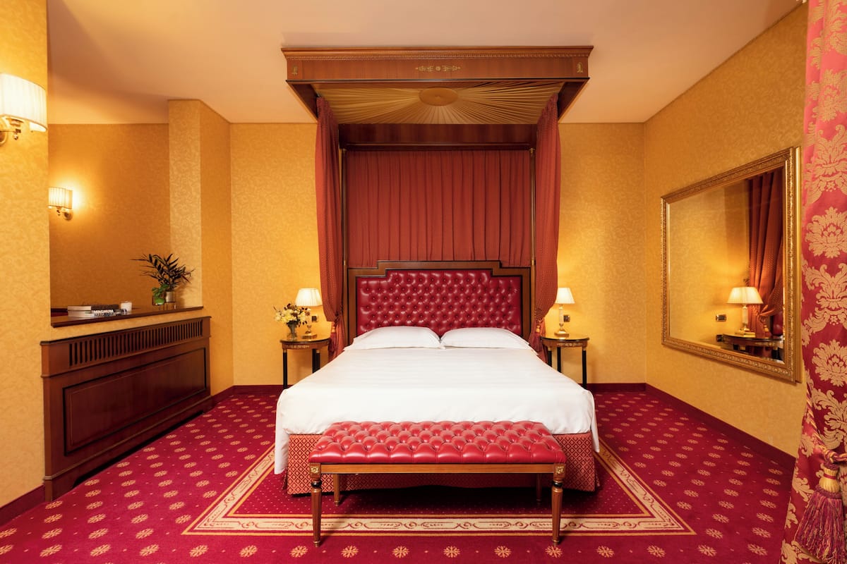A hotel room with a large bed, a bench, a dresser, and a mirror.