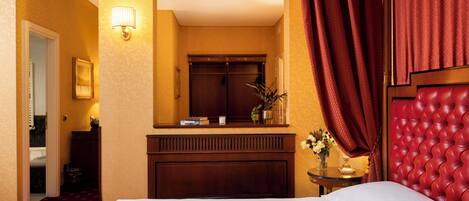 A hotel room with a bed, a wooden dresser, a mirror, a red curtain, and a wall-mounted lamp.