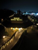 Un HOTEL MAXIM con un letrero llamativo, un acceso pavimentado y un camino bien iluminado hacia la entrada.