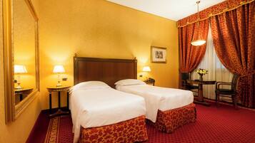 A hotel room with two beds, a large mirror, a desk with a chair, and a window with curtains.