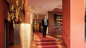 Een man loopt over een tapijtvloer een trap af in een hotelhal, met een grote plantenvaas.