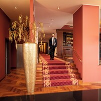 Un hombre camina por una escalera alfombrada en el vestíbulo de un hotel, con un gran jarrón de plantas.