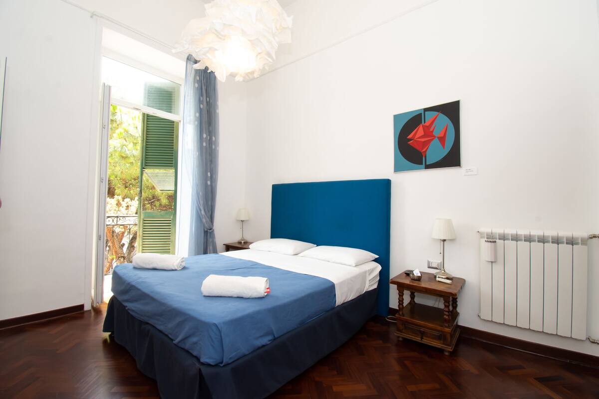 A bedroom with a bed, a nightstand, a lamp, a radiator, and a window with curtains.