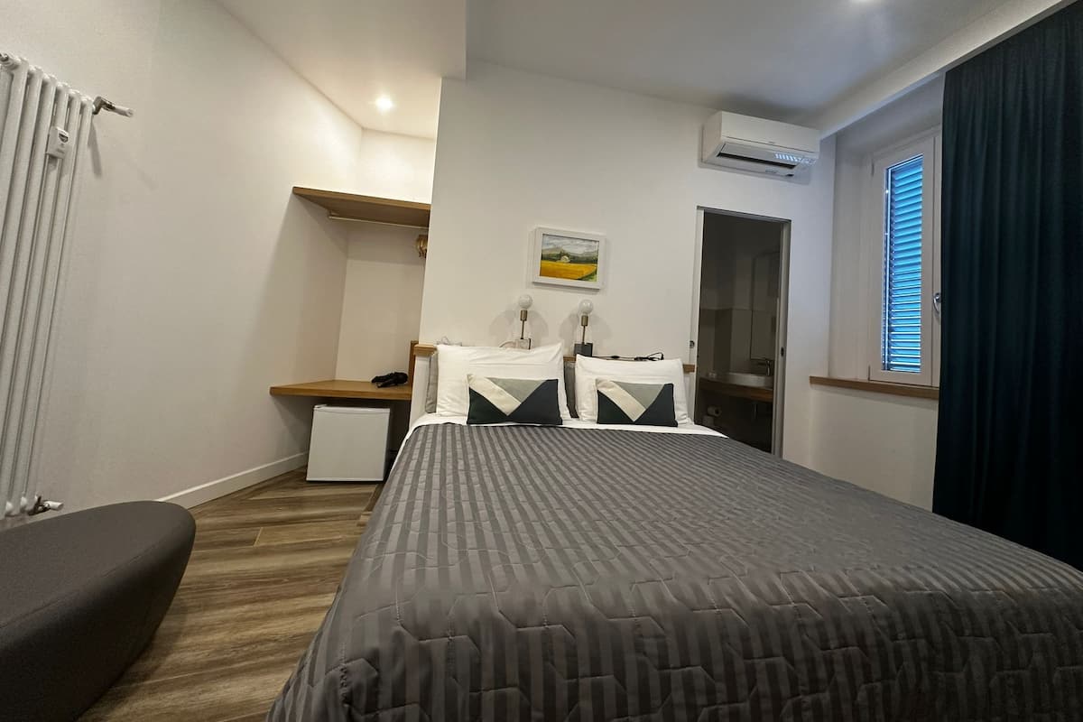 A bedroom with a bed, bedside table, lamp, and a small desk with a chair.