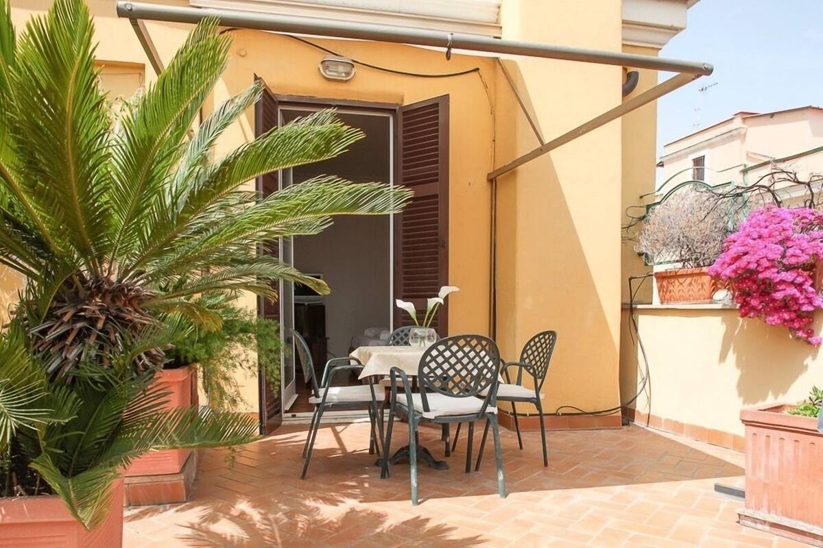 An outdoor patio with a table and chairs, a potted plant, and a wall-mounted flower pot.