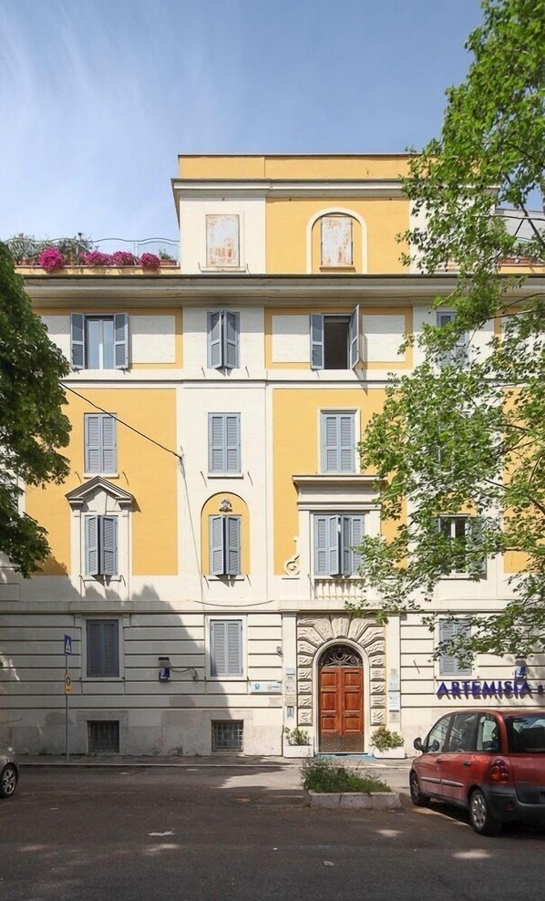 A multi-story building with a yellow facade, a central entrance with a wooden door, and a sign reading "ARTEMISIA". - Astoria Palace (Rome)