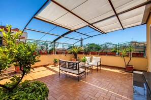 A covered patio with a sofa, chair, and table, surrounded by potted plants and a clear view of the cityscape. - Astoria Palace (Rome)
