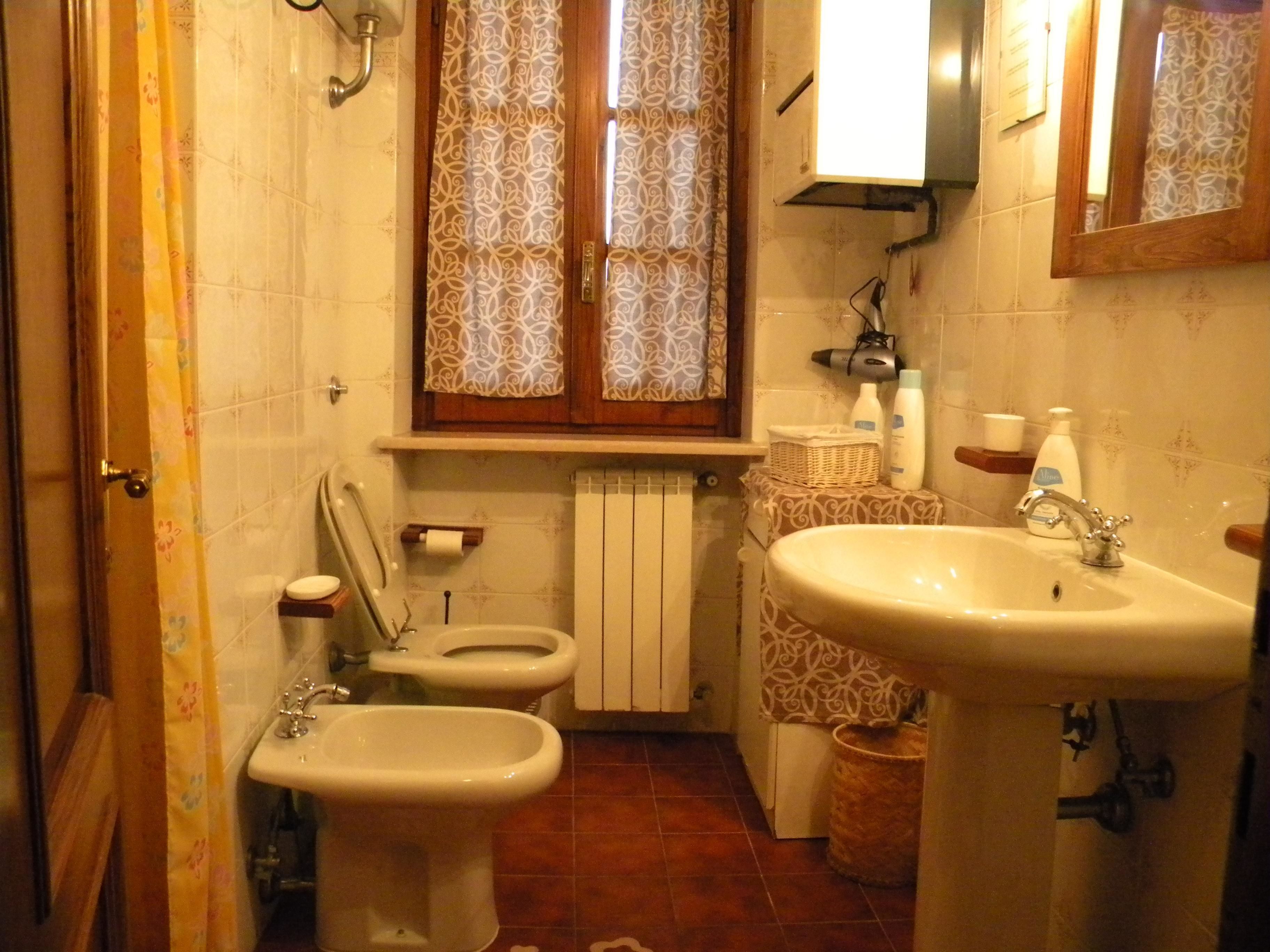 Un baño con dos inodoros, un bidé, un lavabo, un espejo y una ventana con cortinas estampadas.