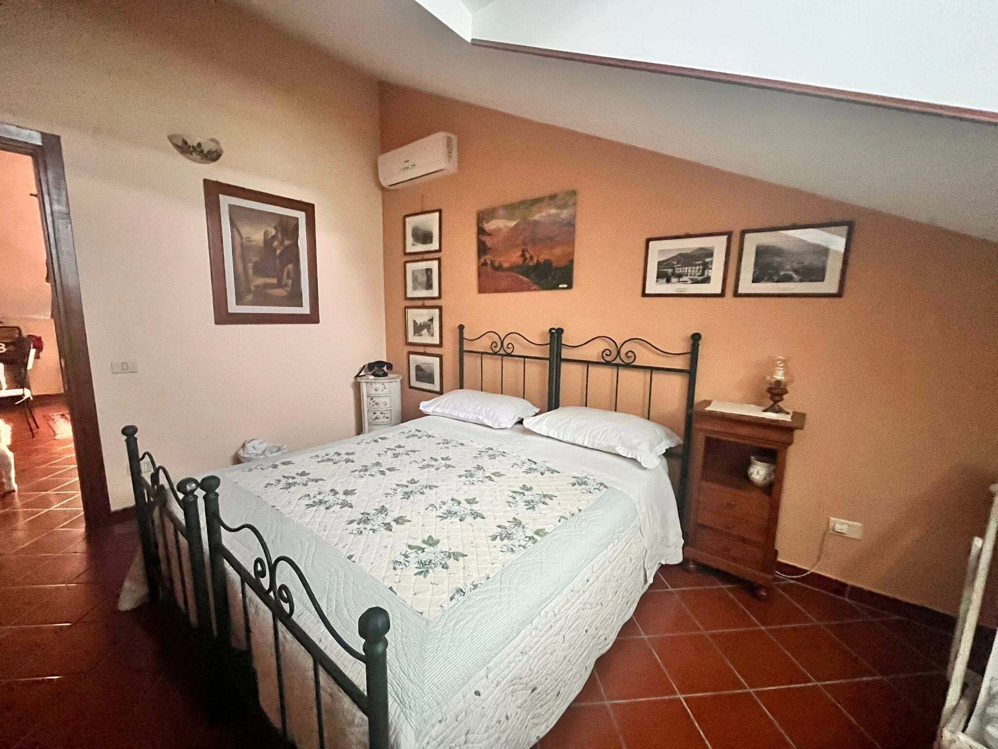 A bedroom with a bed, a nightstand, a wall-mounted air conditioner, and framed pictures.