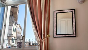 Quarto com vista para edifícios históricos, um espelho emoldurado e cortinas na janela.