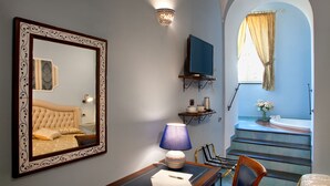 Quarto com um espelho grande, abajur, televisão e vista para um banheiro com banheira e escadas.
