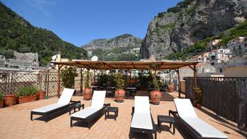 Una terraza en la azotea con sillones de descanso, plantas en macetas y una pérgola.