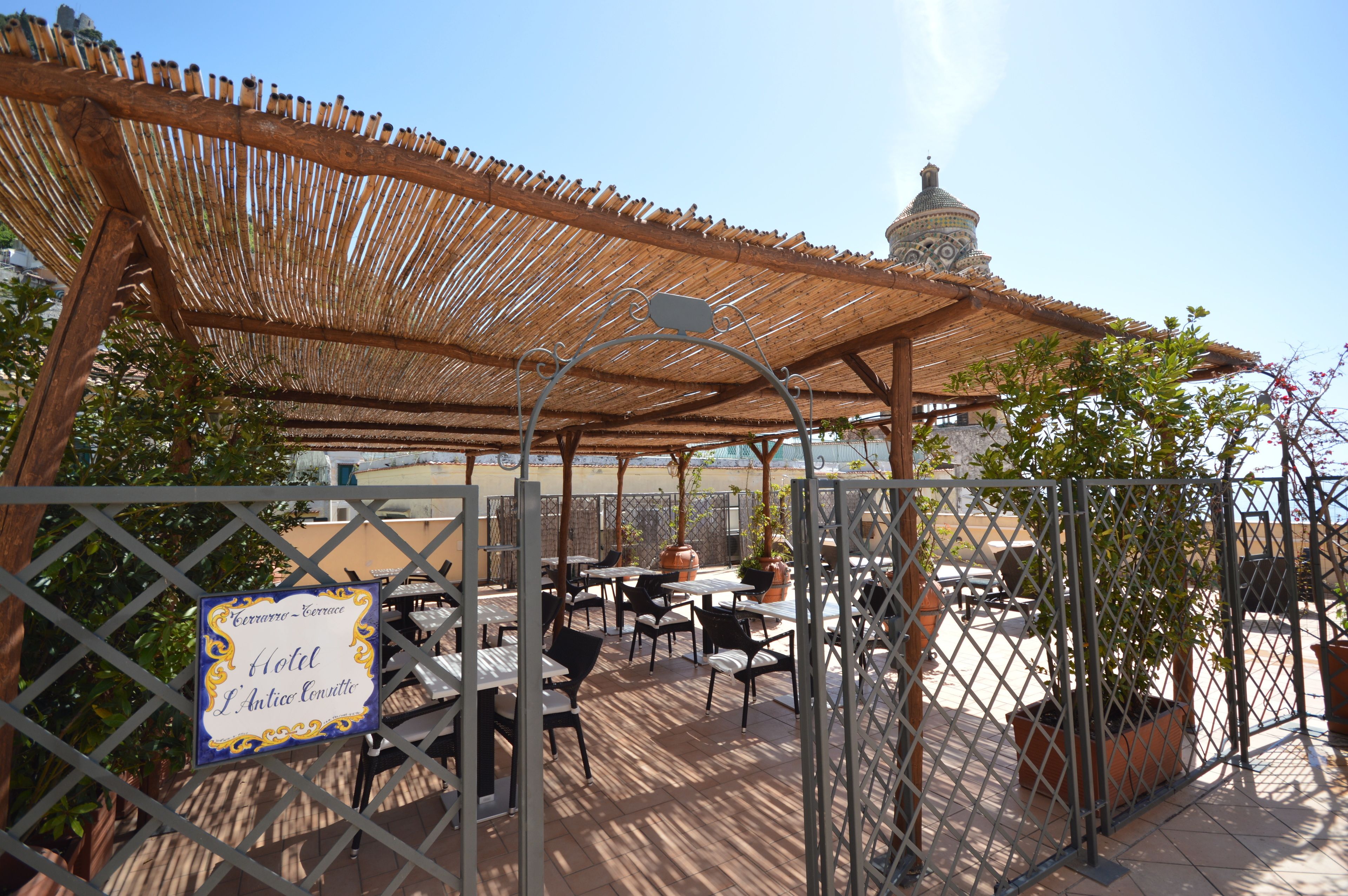 Un área de estar al aire libre con techo, mesas y sillas, un letrero que indica un hotel y una estructura en forma de cúpula al fondo.